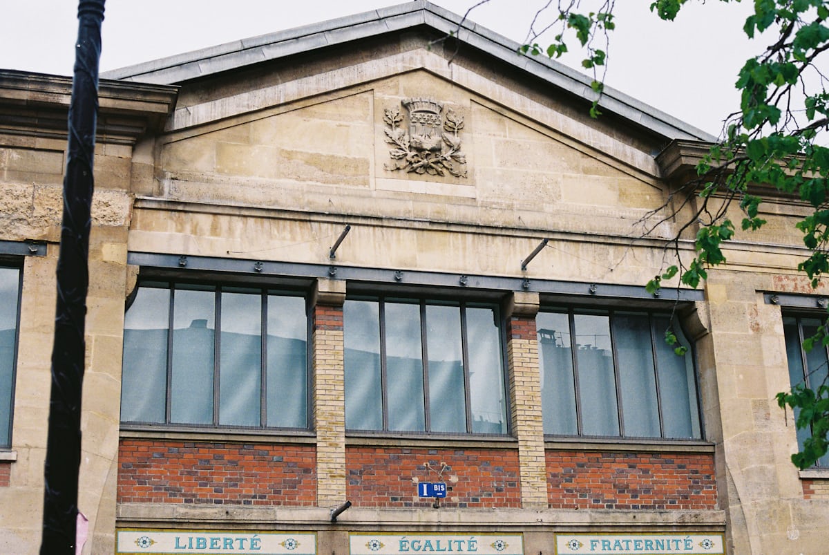 Façade parisienne en pierre et brique, avec de grandes fenêtres sous un fronton sculpté.